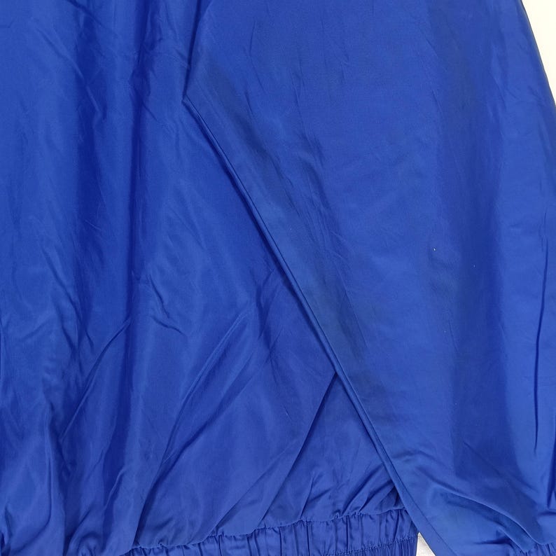 May include: A close-up of a vibrant blue jacket. The jacket's fabric has a slight sheen, and the design includes seams and a gathered hem. The color is consistent throughout, with subtle variations due to the fabric's texture.
