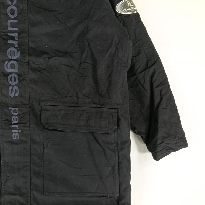 May include: Black jacket with a pocket and the text "courr&egrave;ges paris" vertically down the side. A small patch with the brand logo is on the upper sleeve. The jacket appears to be made of a durable material.