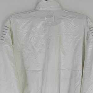 May include: A white, full-zip jacket with a high collar. The jacket has a subtle, textured pattern across the fabric. The shoulders feature three parallel gray stripes. The jacket is made of a lightweight material.