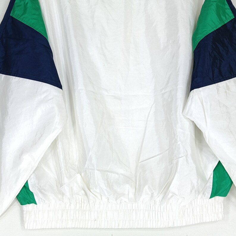 May include: White nylon jacket with green and navy blue color block accents on the sleeves. The jacket has a gathered waist and a full zipper. The jacket is a vintage style.