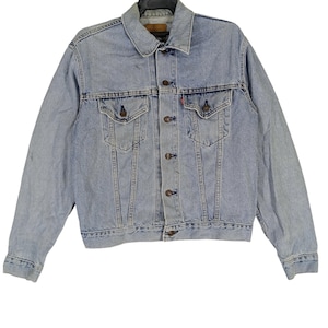 Puede incluir: Una chaqueta vaquera azul claro con cierre de botones y dos bolsillos en el pecho.