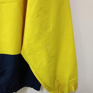 Puede incluir: Primer plano de una chaqueta amarilla y azul marino. La manga de la chaqueta es amarilla, con una secci&oacute;n azul marino en la parte inferior. La tela tiene algunas manchas. La chaqueta est&aacute; hecha de un material ligero.