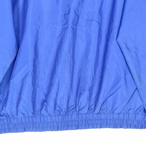 May include: Close-up of a solid periwinkle blue jacket. The jacket has a gathered elastic waistband and a smooth, slightly shiny texture. The fabric is creased, suggesting it is made of a lightweight material.