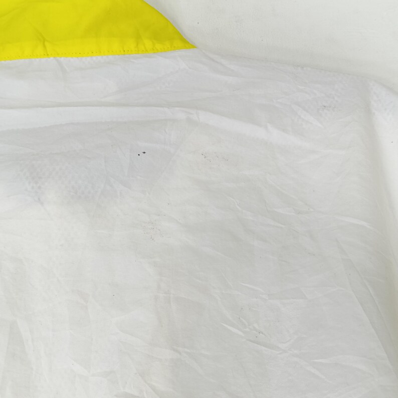 May include: Close-up of a white fabric with a yellow trim. The fabric appears to be thin and slightly translucent, with subtle textures and folds. The yellow trim is a bright, solid color.