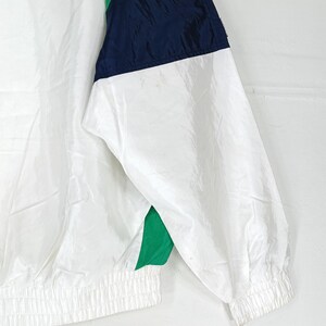 May include: White nylon jacket with navy blue and green accents. The jacket features a color block design on the upper portion of the sleeve and shoulder. The sleeve cuffs and waistline are elasticized.