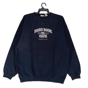 Könnte beinhalten: Marineblaues Hard Rock Cafe Honolulu Sweatshirt. Der weiße Text auf der Vorderseite lautet "Hard Rock Cafe" über "Honolulu". Das Sweatshirt hat einen Rundhalsausschnitt und lange Ärmel. Es hängt an einem schwarzen Kleiderbügel.