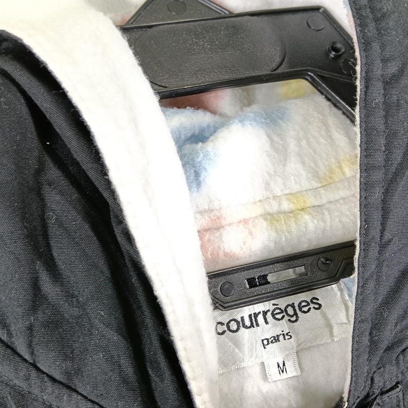 May include: Black jacket with a white fleece-lined hood and a colorful polka-dot pattern. The jacket is hanging on a black hanger. The label reads "courr&egrave;ges paris" with a size "M".