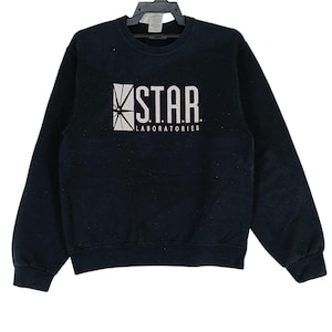 Może przedstawiać: Czarna bluza z okrągłym dekoltem z białym napisem "STAR LABORATORIES". Grafika przedstawia stylizowany wzór gwiazdy. Bluza wykonana jest z miękkiego materiału i ma klasyczny krój.