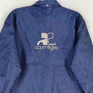 May include: A navy blue jacket with a white logo that says "Courr&egrave;ges" and a stylized "AC" logo.