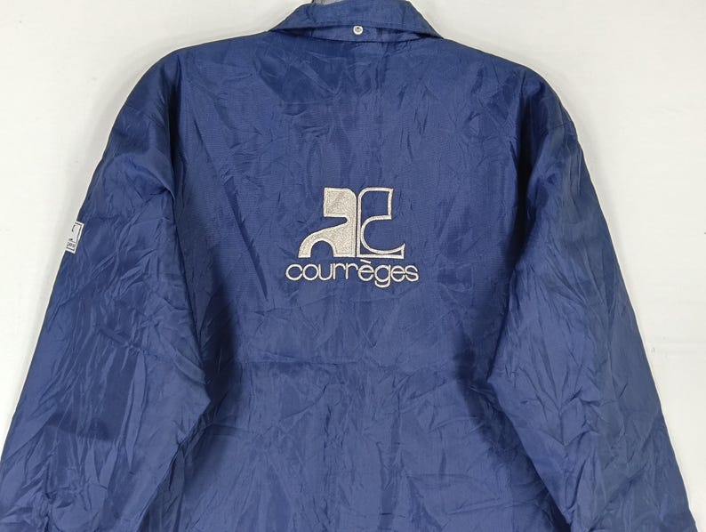 May include: A navy blue jacket with a white logo that says "Courr&egrave;ges" and a stylized "AC" logo.