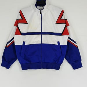 May include: A white, blue, and red track jacket with a zipper closure. The jacket has a geometric pattern with a white background and blue and red accents.