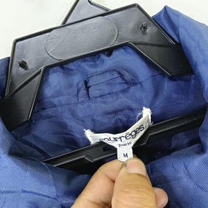 May include: A blue jacket with a white label that says "Mur&egrave;ges Paris" and "M" on it.