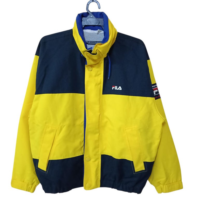 Puede incluir: Chaqueta Fila vintage en amarillo y azul marino. La chaqueta tiene un cuello alto, una cremallera completa y el logotipo de Fila en el pecho. La chaqueta presenta un dise&ntilde;o de bloques de color con amarillo en la mitad inferior y azul marino en la mitad superior.