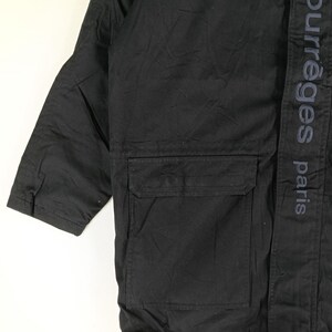 May include: Black jacket with a large pocket and the text "courreges paris" printed vertically on the right side. The jacket has a simple, utilitarian design.