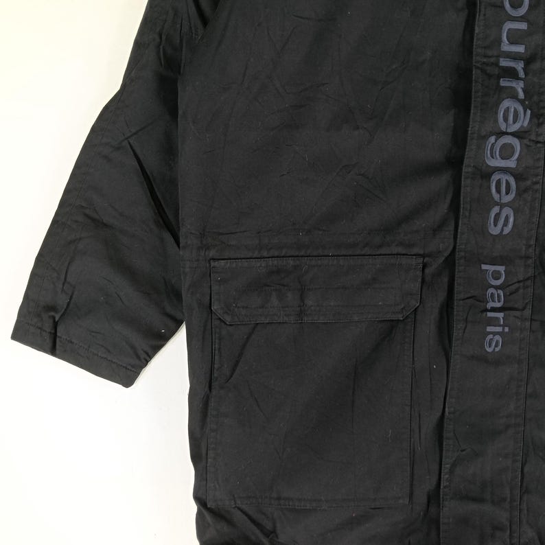 May include: Black jacket with a large pocket and the text "courreges paris" printed vertically on the right side. The jacket has a simple, utilitarian design.