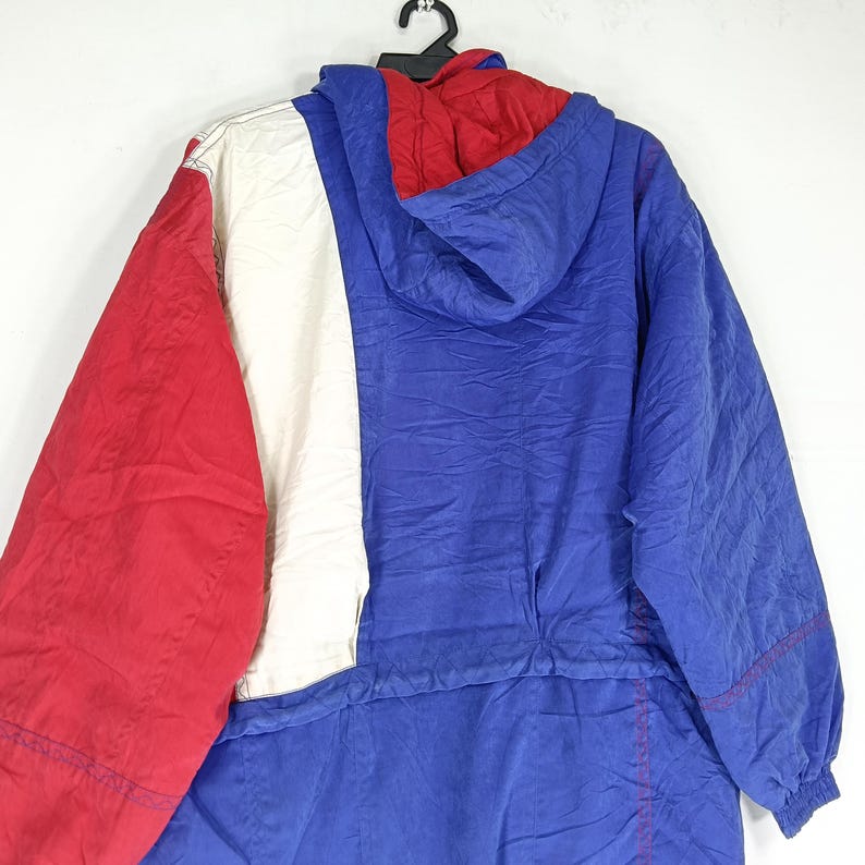 May include: A vintage color-block jacket in red, white, and blue. The jacket features a hood and a full-length zipper. The design includes a red hood, a white vertical stripe, and a blue body. The jacket is hanging on a black hanger.