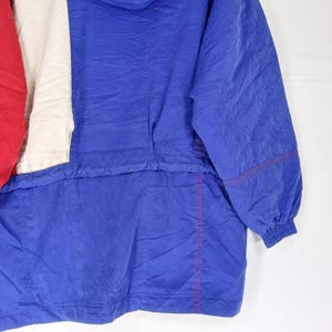 May include: A vintage blue, red, and white anorak jacket. The jacket features a color block design with a red panel on the left, a white panel in the center, and a blue panel on the right. The jacket has a hood and a drawstring at the waist.