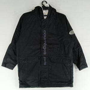 May include: Black hooded jacket with the text "courr&egrave;ges paris" vertically down the front. The jacket has two front pockets and a logo patch on the sleeve. The jacket is hanging on a white hanger.