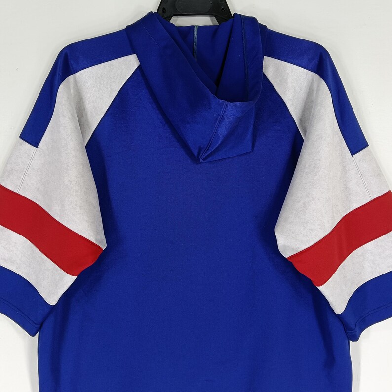 K&ouml;nnte beinhalten: Ein blaues Kapuzenpullover mit wei&szlig;en und roten Streifen&auml;rmeln. Die &Auml;rmel sind im Raglan-Stil.