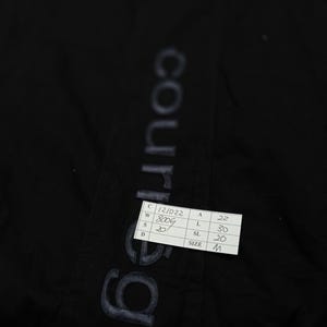 May include: Black garment with the word "courreges" printed vertically in a faded, light color. A small white tag with black text is attached, displaying measurements and the size "M".