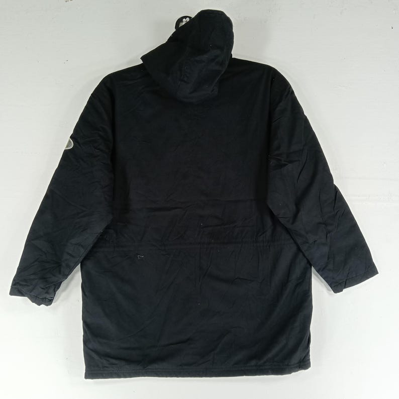 May include: A black hooded parka jacket with long sleeves. The jacket has a drawstring waist and a small logo on the left sleeve. The hood is attached and the jacket is made of a durable material.