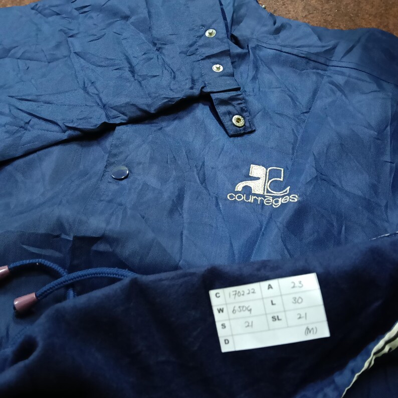 May include: A navy blue jacket with a white logo that says "Courreges" and a white tag with size information. The tag says "C 170222 A 25 W 6504 L 30 SL 21 D (M)"