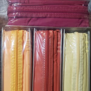 May include: Bed sheet sets in peach, burgundy, orange, and yellow. Each set is packaged in a clear plastic case with a matching zip closure. The sheets appear to be made of a soft, smooth fabric, suitable for a double or king-size bed.