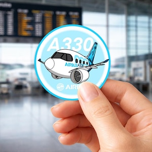 Peut inclure: Un autocollant rond avec un dessin animé d'un avion Airbus A330, avec le texte "A330" et "Airbus A330". L'autocollant a un bord bleu clair et est tenu devant un terminal d'aéroport.