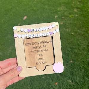 May include: A wooden teacher appreciation plaque with the text "HAPPY TEACHER APPRECIATION THANK YOU FOR EVERYTHING YOU DO! LOVE, HOLLIS 2025-2026". The plaque has a pink apple and decorative beads.