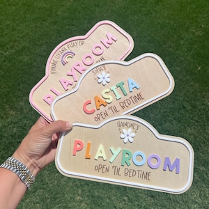 Puede incluir: Tres letreros de madera personalizados con bordes redondeados y letras coloridas en relieve. Los letreros incluyen los textos KIMMIE LIYANA KHAYER PLAYROOM, SOFIA'S CASITA OPEN 'TIL BEDTIME y HAINLINE'S PLAYROOM OPEN 'TIL BEDTIME, decorados con iconos de arco&iacute;ris y flores.