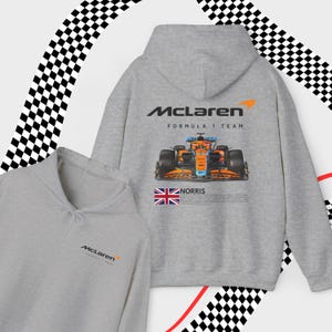 May include: Gray hooded sweatshirt with the McLaren Formula 1 team logo and a racing car graphic on the back. The front of the sweatshirt has a smaller McLaren logo.