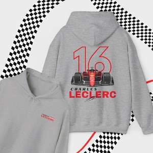 Puede incluir: Sudadera con capucha gris con un coche de carreras rojo y el n&uacute;mero 16 impreso en la espalda. El texto "Charles Leclerc" est&aacute; impreso debajo del coche con una firma.