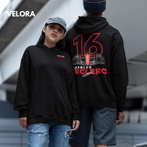 Puede incluir: Dos sudaderas con capucha negras con un gr&aacute;fico de coche de carreras rojo en la espalda. La sudadera de la derecha tiene el n&uacute;mero 16 y el nombre "Charles Leclerc" impreso en ella.