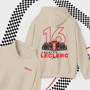 Puede incluir: Sudadera beige con un n&uacute;mero 16 rojo y un coche de carreras Ferrari rojo en la parte posterior. El texto "Charles Leclerc" est&aacute; impreso debajo del coche. La parte delantera de la sudadera tiene el texto "Charles Leclerc" impreso en rojo.