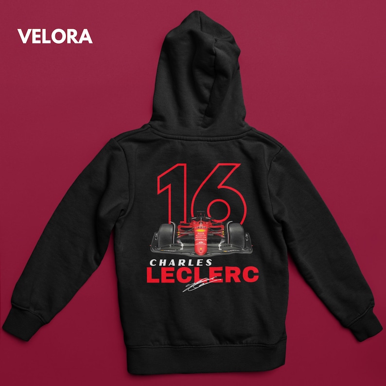 Puede incluir: Sudadera con capucha negra con un gr&aacute;fico de coche de carreras rojo y blanco en la parte posterior. El coche tiene el n&uacute;mero 16 y el texto "CHARLES LECLERC" con una firma.
