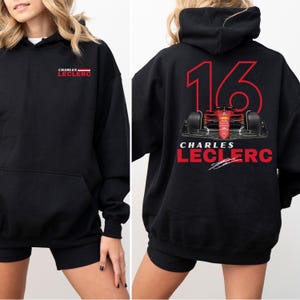 Puede incluir: Sudadera con capucha negra con un gráfico rojo y blanco de un coche de carreras y el texto "CHARLES LECLERC" y el número "16" en la espalda.