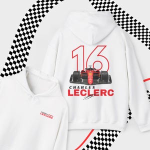 Puede incluir: Sudadera con capucha blanca con un coche de carreras rojo y el n&uacute;mero 16 impreso en la espalda. El texto "Charles Leclerc" est&aacute; impreso debajo del coche. La parte delantera de la sudadera tiene el texto "Charles Leclerc" impreso en rojo.