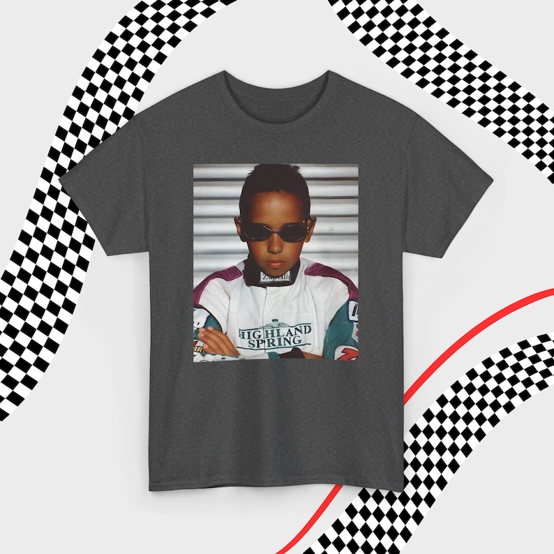 A gray t-shirt laid flat against a dynamic background of black-and-white checkered patterns and curved red lines. Centered on the shirt is a nostalgic photo print of a young Lewis Hamilton wearing sunglasses, arms crossed, and a vintage racing jacket with "Highland Spring" text. The brand name "VELORA" is displayed in the top-left corner in black, bold sans-serif font.