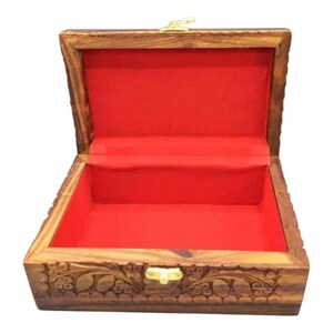 Könnte beinhalten: Eine Holzkiste mit einem geschnitzten Blumenmuster und einem roten Samt-Innenraum. Die Kiste hat einen Deckel mit Scharnieren und einen Messingverschluss.