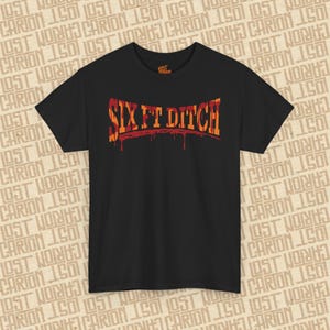 May include: Black t-shirt with the text "SIX FT DITCH" in orange and red, with a dripping effect. The shirt has a crew neck and short sleeves. The brand logo is visible on the upper right.