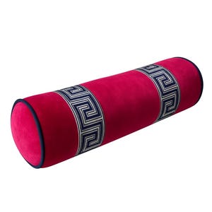 May include: A cylindrical decorative pillow in a vibrant fuchsia color. The pillow features a navy blue trim and two bands of a Greek key pattern in navy and white. The pillow is designed for home decor.