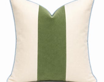 May include: A square throw pillow featuring a wide, vertical olive green center stripe flanked by two cream-colored side panels. The pillow is finished with a light blue piping trim along all four edges, creating a clean and structured appearance.