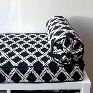 May include: A black and white patterned bench with a matching bolster pillow. The diamond pattern is a repeating design on the seat and pillow. The bench is on a white frame.