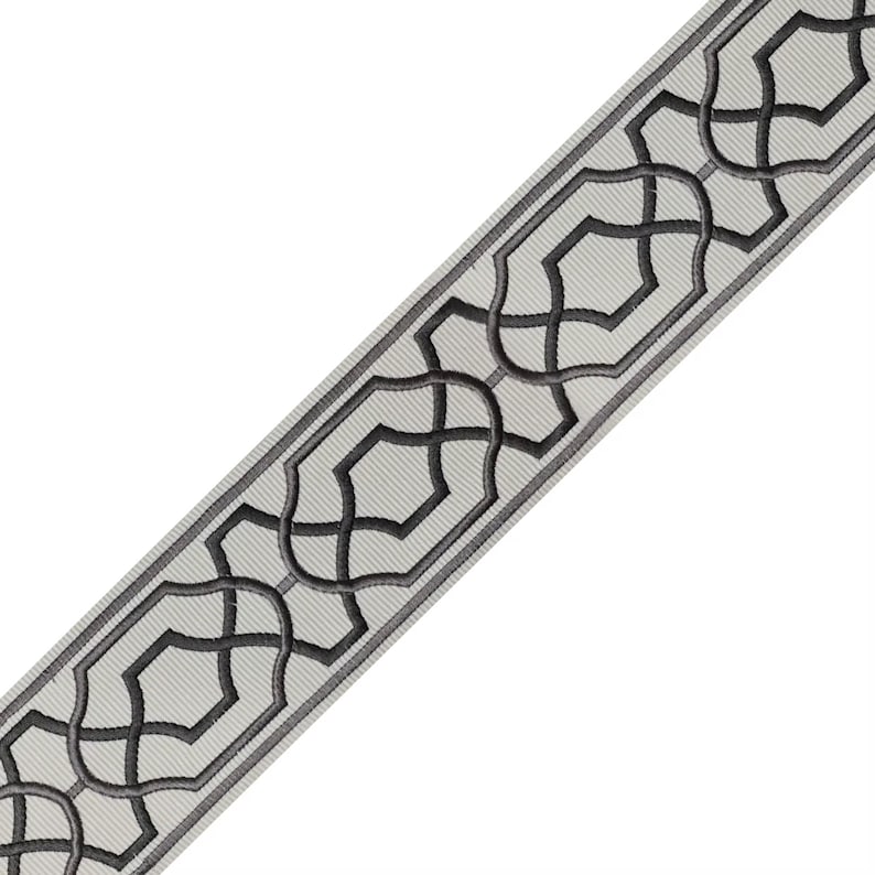 May include: A decorative trim with a repeating geometric pattern. The trim features a light gray background with a dark gray, stylized interlocking design. The edges are outlined in a darker gray, creating a defined border. This trim is suitable for various craft and design projects.