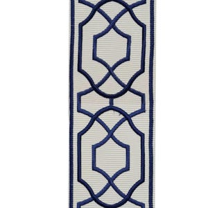 May include: Decorative ribbon featuring a repeating geometric pattern in navy blue on a cream-colored background. The design includes interlocking shapes and lines, creating a symmetrical and elegant look. The ribbon has a textured, ribbed surface.