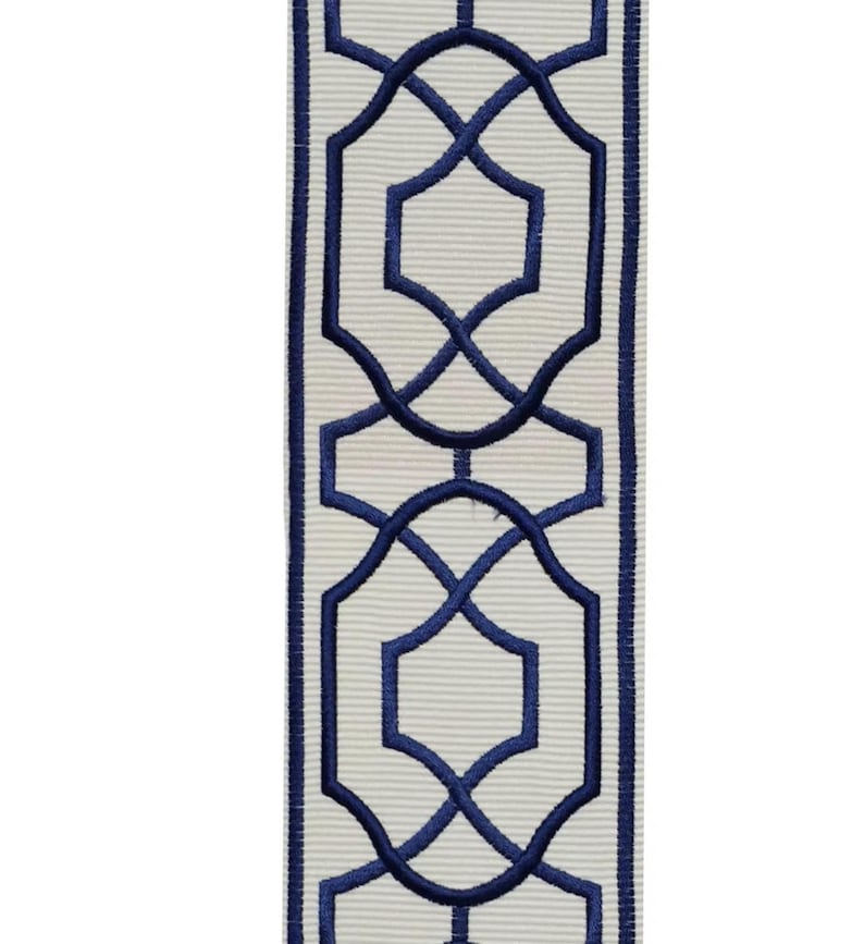 May include: Decorative ribbon featuring a repeating geometric pattern in navy blue on a cream-colored background. The design includes interlocking shapes and lines, creating a symmetrical and elegant look. The ribbon has a textured, ribbed surface.