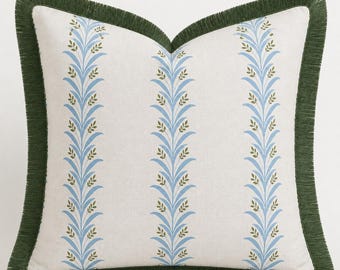 Può includere: Un cuscino quadrato con base bianco sporco caratterizzato da tre colonne verticali di motivi a foglie color azzurro e verde oliva. I bordi del cuscino sono rifiniti con una frangia verde scuro che incornicia l'intera forma quadrata.