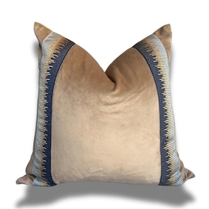 May include: A tan velvet pillow with a blue, gold, and white geometric patterned trim.