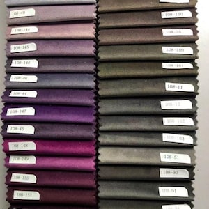May include: A collection of fabric swatches in various shades of purple, gray, and brown. Each swatch is labeled with a white tag. The swatches are arranged in neat rows, showcasing a range of colors and textures, suitable for upholstery or interior design projects.