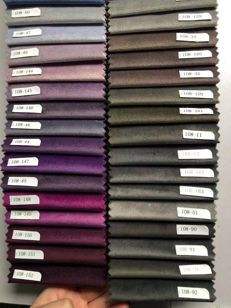 May include: A collection of fabric swatches in various shades of purple, gray, and brown. Each swatch is labeled with a white tag. The swatches are arranged in neat rows, showcasing a range of colors and textures, suitable for upholstery or interior design projects.